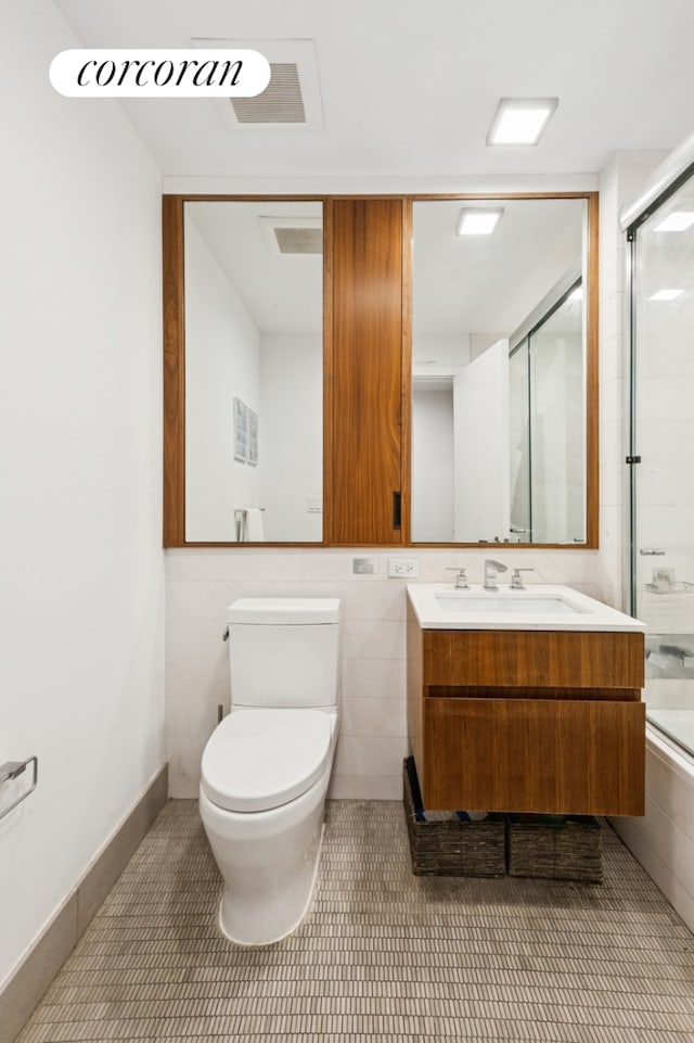 full bathroom featuring double vanity, toilet, tile patterned floors, a shower with shower door, and a sink