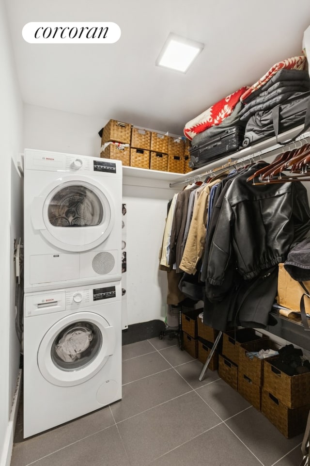 laundry room with laundry area, dark tile patterned flooring, and stacked washer / drying machine