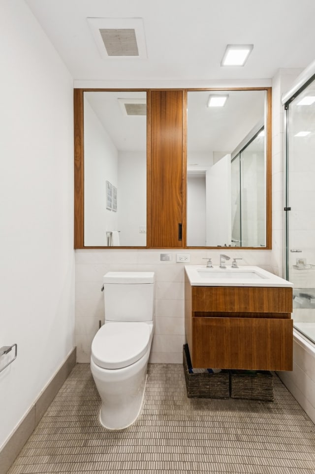 full bathroom featuring double vanity, visible vents, toilet, a shower with shower door, and a sink