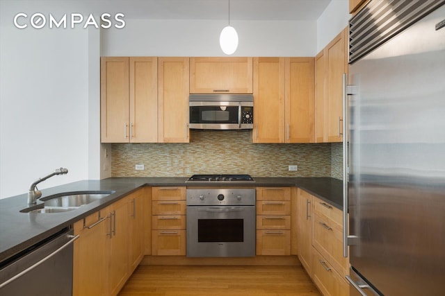 kitchen with appliances with stainless steel finishes, dark countertops, a sink, and tasteful backsplash