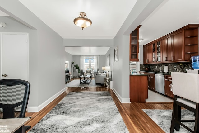 interior space with stainless steel dishwasher, dark countertops, open shelves, wood finished floors, and backsplash
