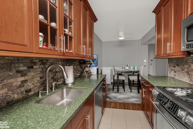 kitchen with dark stone countertops, light tile patterned floors, a sink, tasteful backsplash, and appliances with stainless steel finishes
