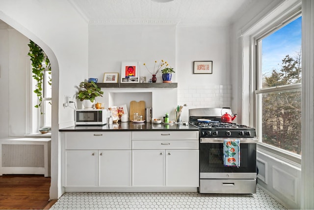 kitchen with dark countertops, radiator, gas range, decorative backsplash, and arched walkways