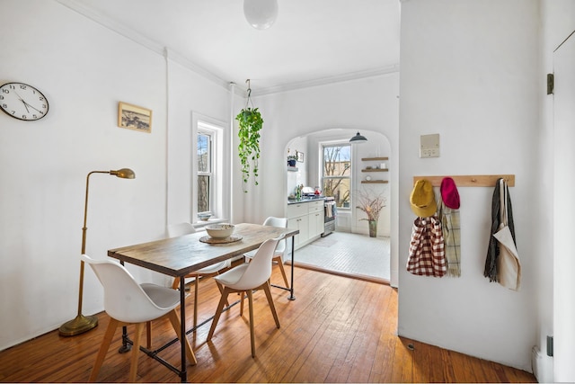 dining space with light wood finished floors, ornamental molding, and arched walkways