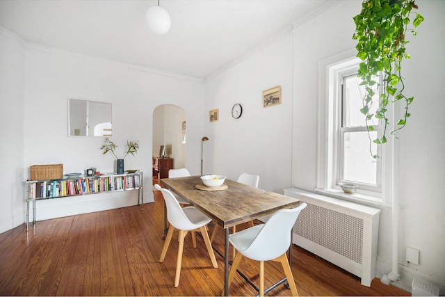 dining area with radiator heating unit, crown molding, arched walkways, and wood finished floors