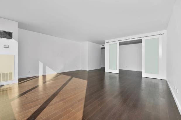 interior space featuring dark wood-style floors, a barn door, visible vents, and baseboards