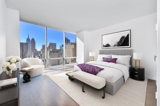 bedroom with expansive windows, baseboards, wood finished floors, and a city view