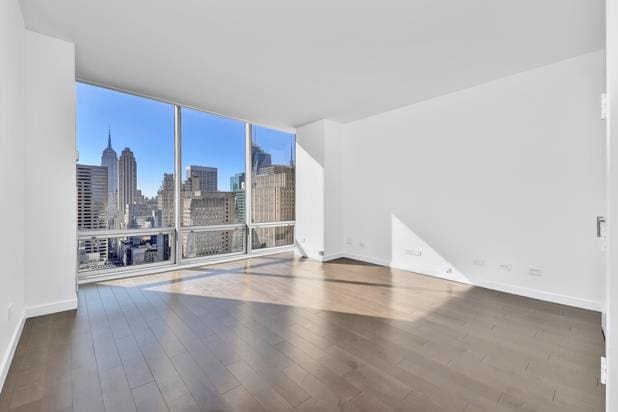 unfurnished room featuring floor to ceiling windows, a city view, baseboards, and wood finished floors