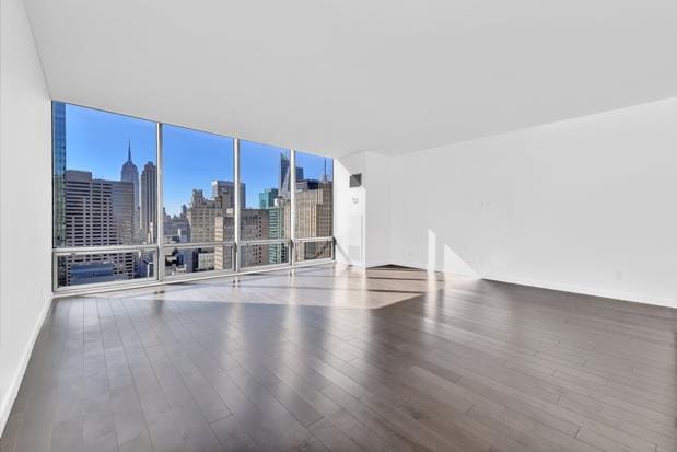 unfurnished room with baseboards, a city view, wood finished floors, and floor to ceiling windows