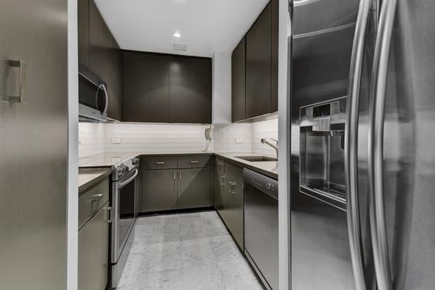 kitchen with stainless steel appliances, a sink, marble finish floor, light countertops, and decorative backsplash