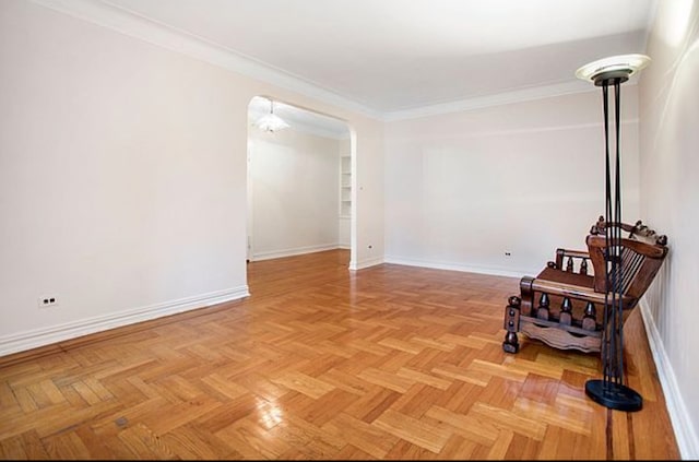 unfurnished room featuring arched walkways, crown molding, and baseboards