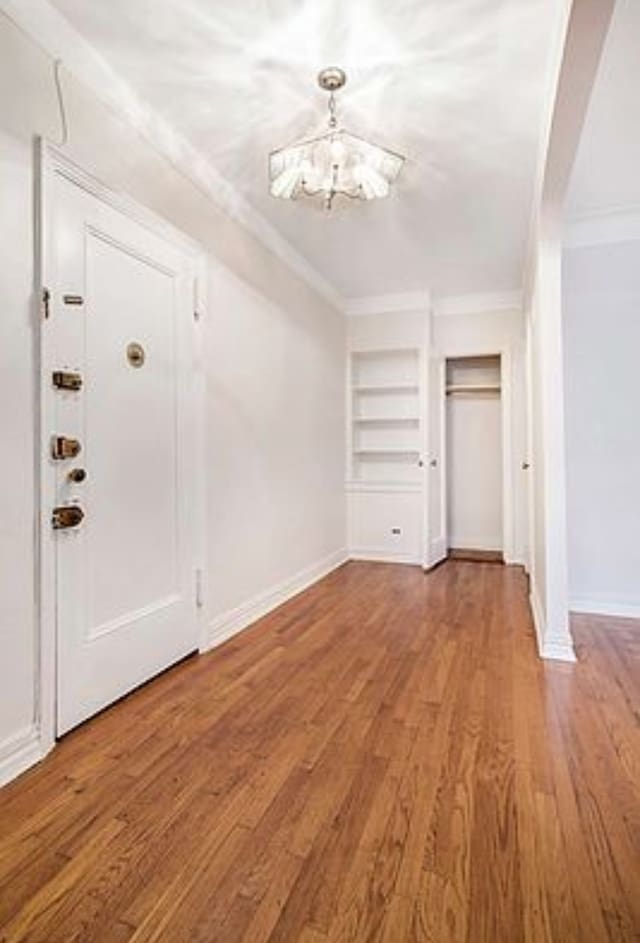 foyer entrance with a chandelier, crown molding, wood finished floors, and baseboards