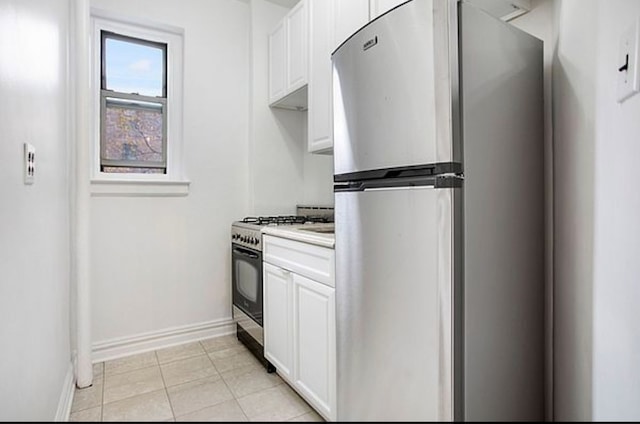 kitchen featuring gas range oven, freestanding refrigerator, white cabinetry, baseboards, and light countertops