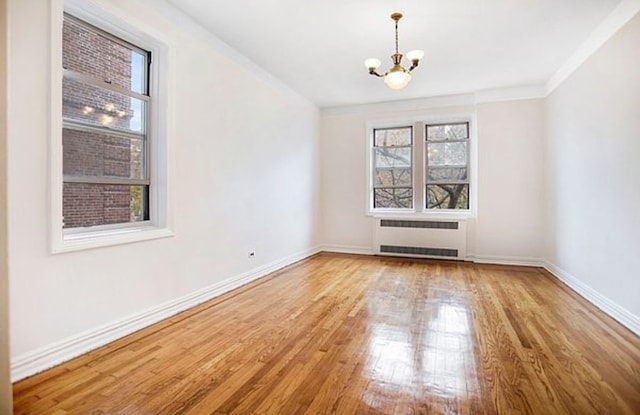 spare room with radiator heating unit, a chandelier, wood finished floors, and baseboards