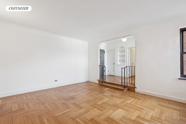 empty room with visible vents, built in shelves, radiator heating unit, arched walkways, and baseboards