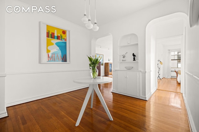 dining space featuring baseboards, arched walkways, built in features, and wood finished floors