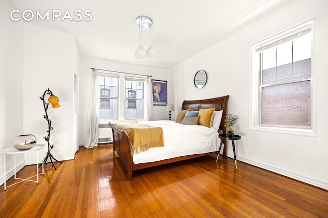 bedroom with baseboards, hardwood / wood-style floors, and radiator heating unit