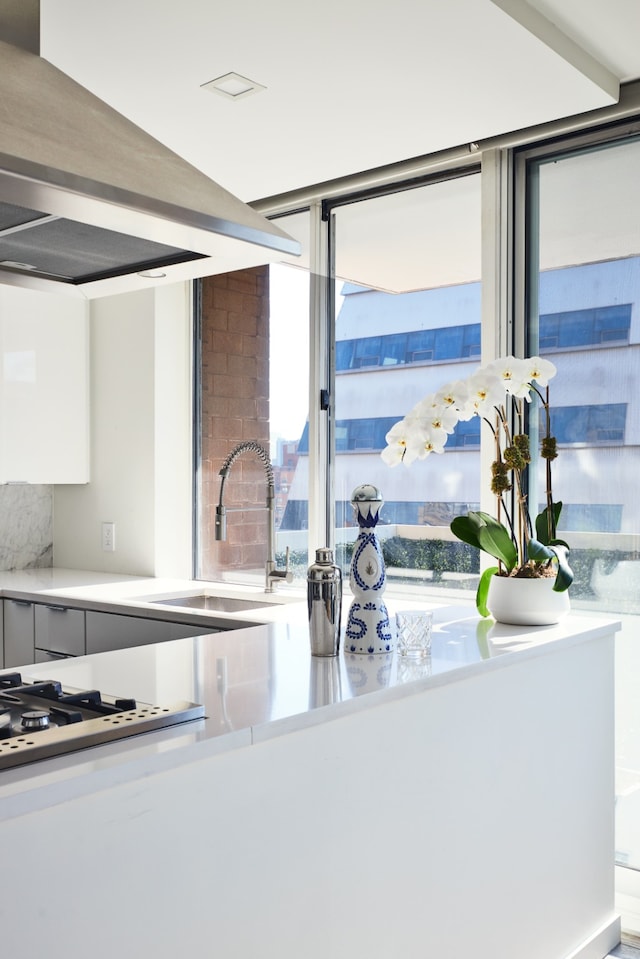 kitchen with white cabinets, a sink, light countertops, wall chimney exhaust hood, and stainless steel gas stovetop