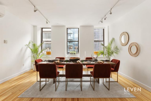 dining space featuring baseboards, a wall mounted air conditioner, wood finished floors, and rail lighting