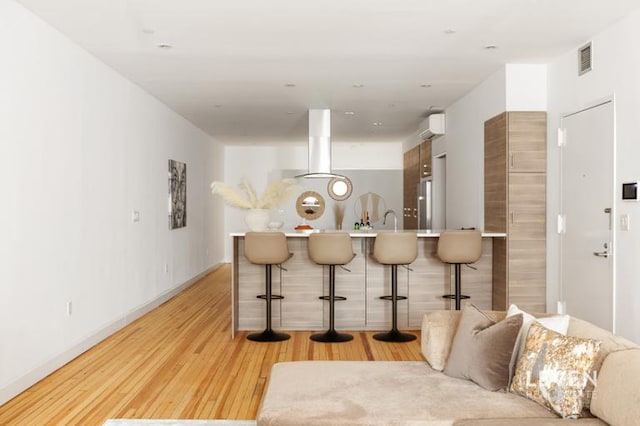bar with island range hood, freestanding refrigerator, light wood-style floors, an AC wall unit, and visible vents