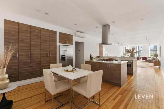 kitchen with a wall unit AC, stainless steel appliances, open floor plan, wall chimney range hood, and a peninsula