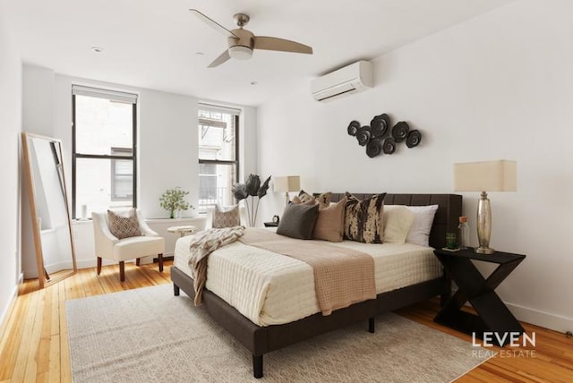 bedroom with an AC wall unit, a ceiling fan, hardwood / wood-style flooring, and baseboards