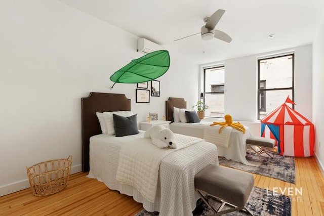 bedroom featuring hardwood / wood-style floors, baseboards, a wall unit AC, and a ceiling fan