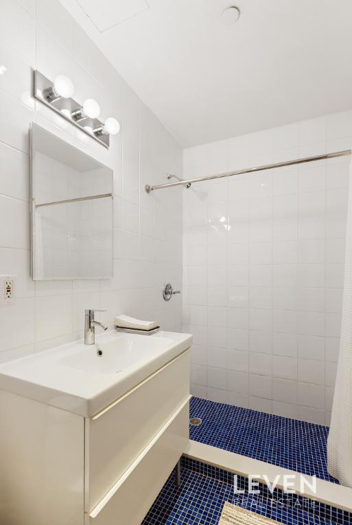 bathroom featuring tasteful backsplash, vanity, tile walls, and tiled shower