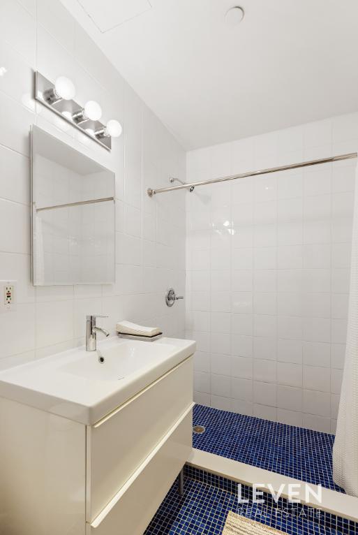 bathroom featuring tiled shower, tile walls, tile patterned floors, vanity, and backsplash