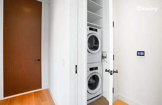 laundry area with light wood finished floors and stacked washer / drying machine