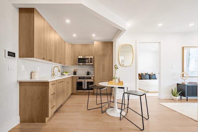 kitchen with stainless steel appliances, light countertops, light brown cabinets, a sink, and modern cabinets