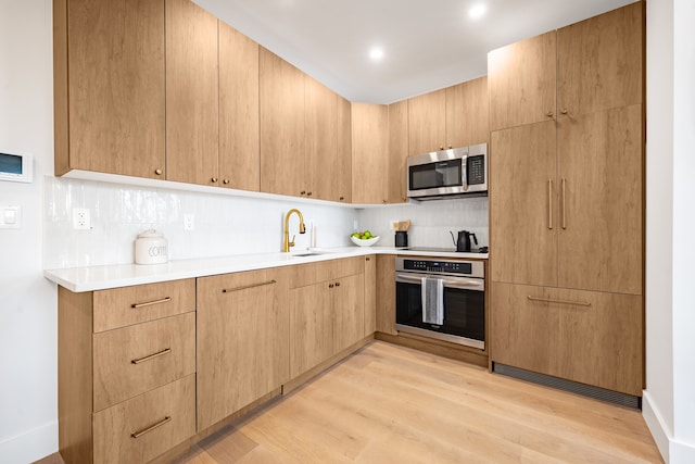 kitchen with stainless steel appliances, a sink, light wood finished floors, and tasteful backsplash