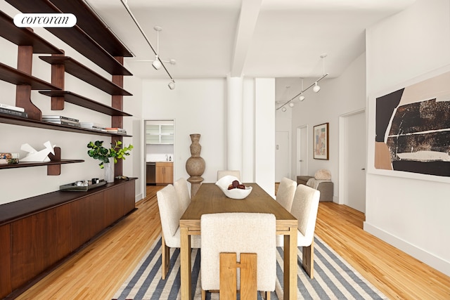 dining area with baseboards, light wood finished floors, a towering ceiling, and track lighting