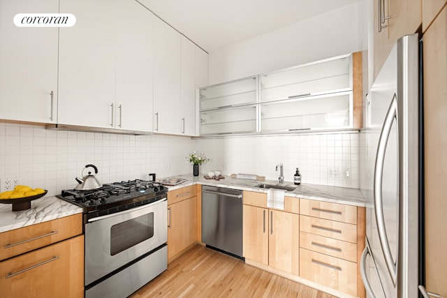 kitchen with stainless steel appliances, a sink, light stone counters, and light wood finished floors