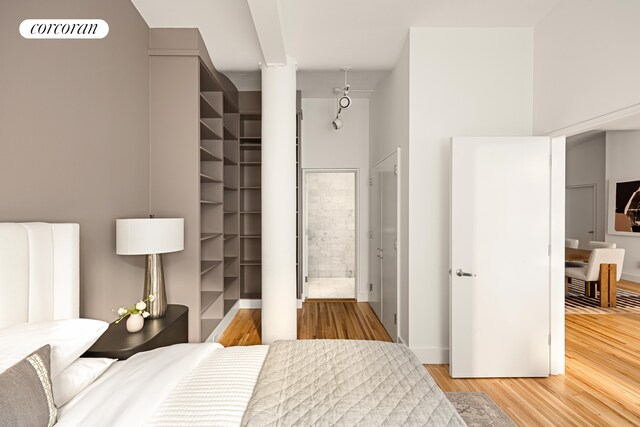 bedroom featuring baseboards, a spacious closet, ensuite bath, and wood finished floors