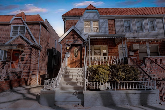 multi unit property featuring brick siding, a porch, and a tile roof