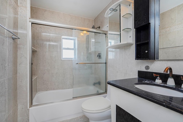 bathroom featuring combined bath / shower with glass door, toilet, tile walls, and vanity