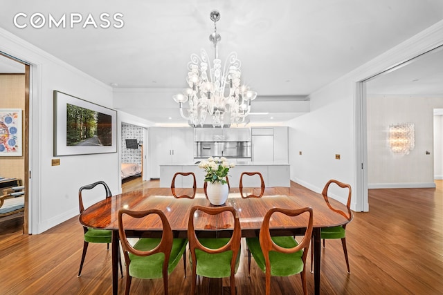 dining room with light wood-style floors, a chandelier, ornamental molding, and baseboards