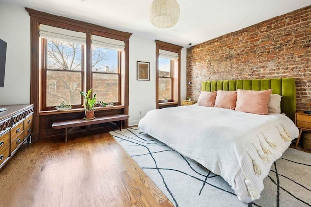 bedroom with light wood finished floors, brick wall, and baseboards