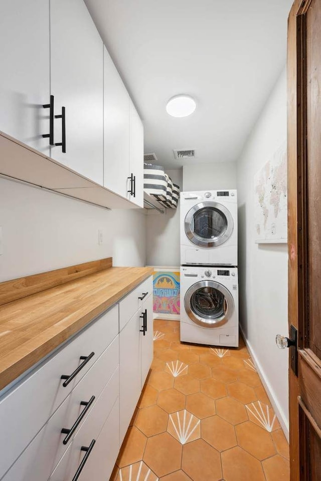 laundry area with light tile patterned flooring, stacked washer and dryer, visible vents, baseboards, and cabinet space