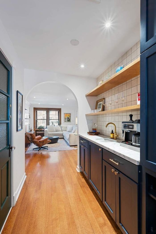 kitchen featuring backsplash, open shelves, light wood-type flooring, arched walkways, and a sink