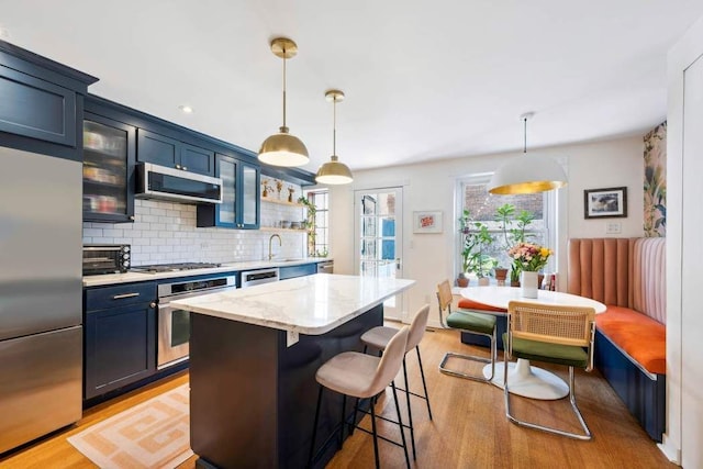 kitchen with tasteful backsplash, glass insert cabinets, appliances with stainless steel finishes, a kitchen breakfast bar, and light wood-style floors