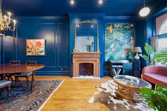 sitting room featuring a large fireplace, ornamental molding, wood finished floors, a decorative wall, and a notable chandelier