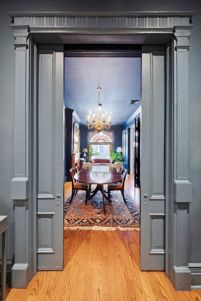 dining room with light wood-type flooring, crown molding, visible vents, and a notable chandelier