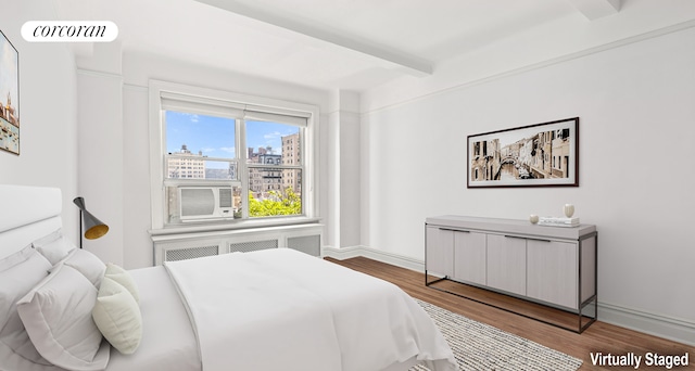 bedroom featuring visible vents, wood finished floors, baseboards, a view of city, and radiator