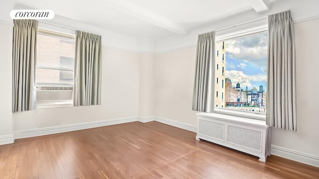spare room with baseboards, beamed ceiling, wood finished floors, and radiator