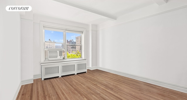 unfurnished room with radiator heating unit, baseboards, wood finished floors, visible vents, and a city view