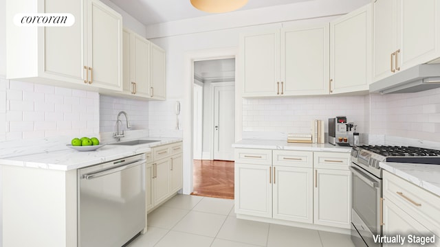 kitchen featuring light stone countertops, under cabinet range hood, a sink, backsplash, and stainless steel appliances