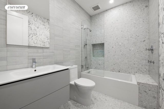full bathroom featuring toilet, tile walls, visible vents, vanity, and tub / shower combination