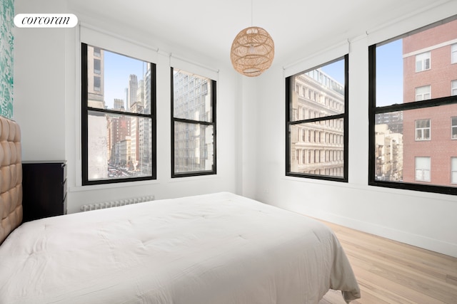 bedroom with radiator, a city view, wood finished floors, and baseboards